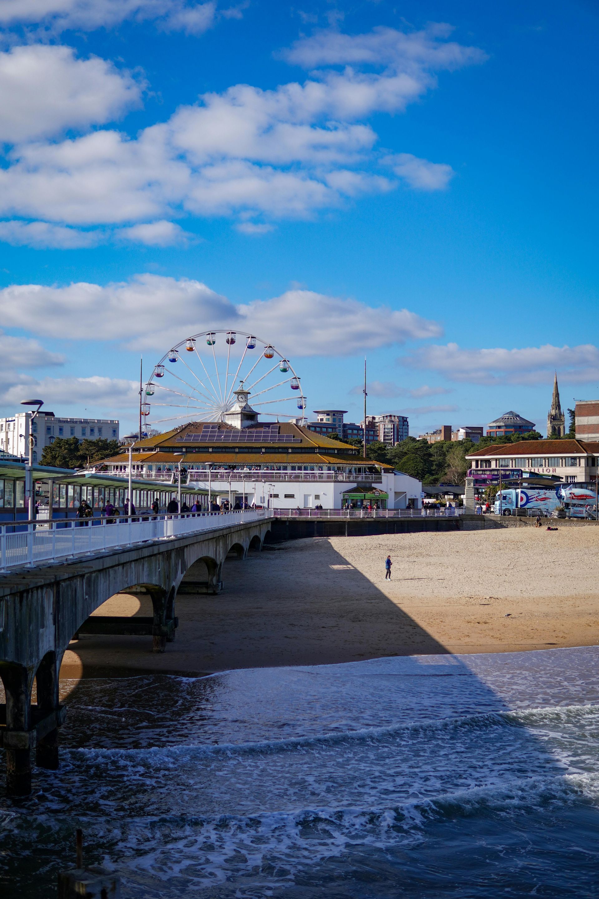 Pier with Ferris wheel and seaside buildings under a bright blue sky