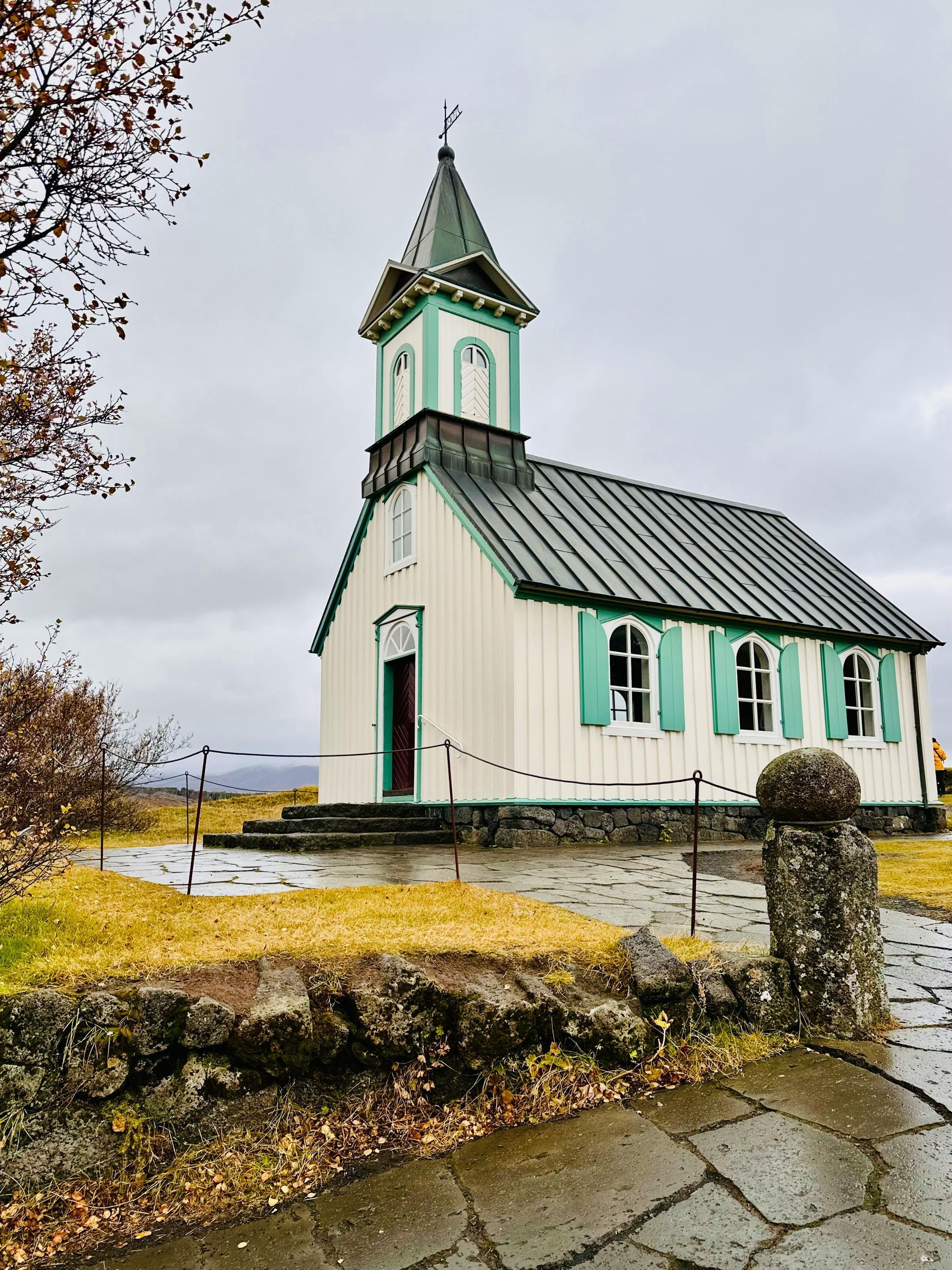 White and green church with steeple on a hill. Stone path and cloudy sky.