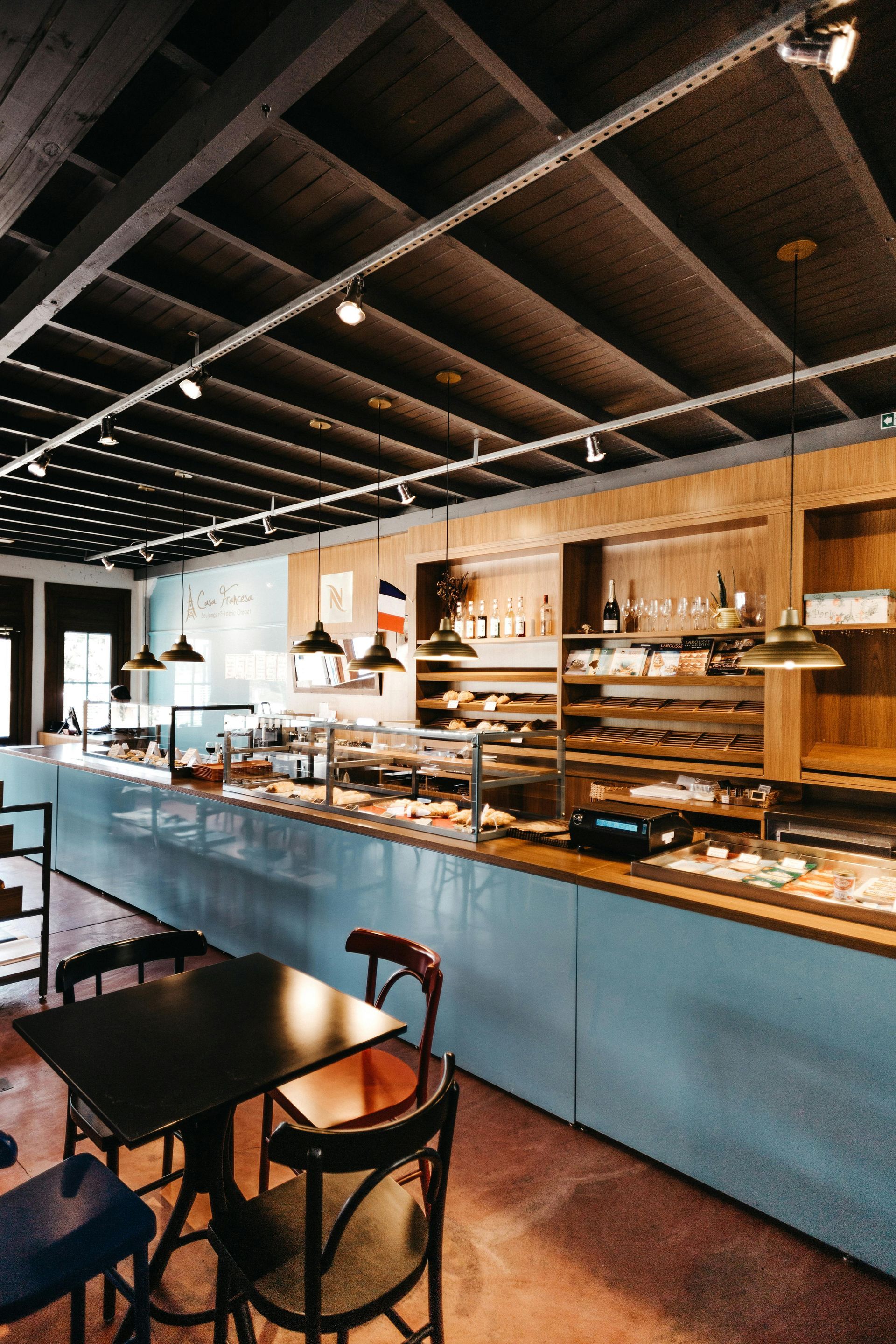 A person in a large rainbow-colored headdress and matching outfit waves at a Pride parade, smiling at the camera.