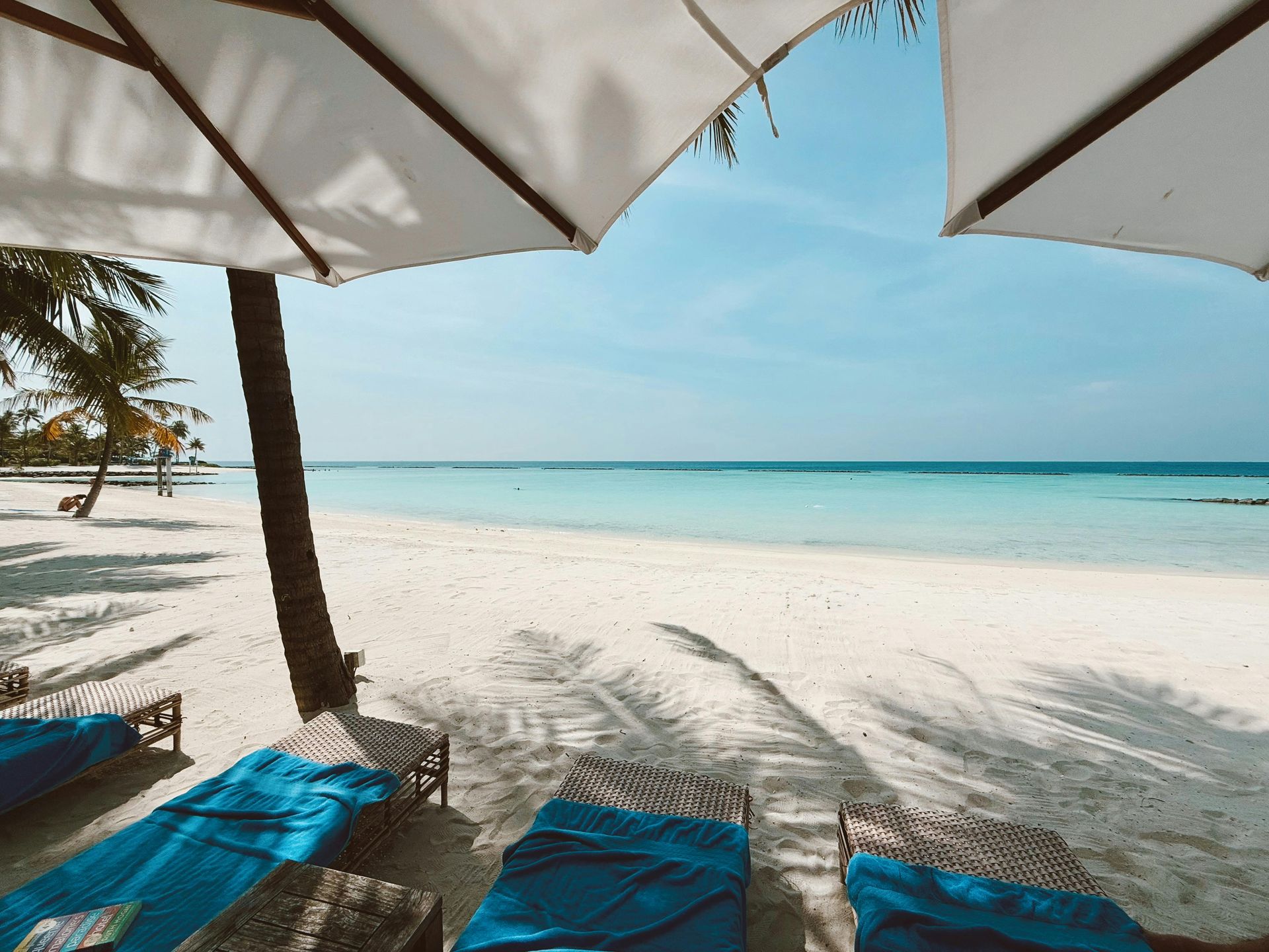 Beach scene with white sand, turquoise water, sun umbrellas, and blue lounge chairs.