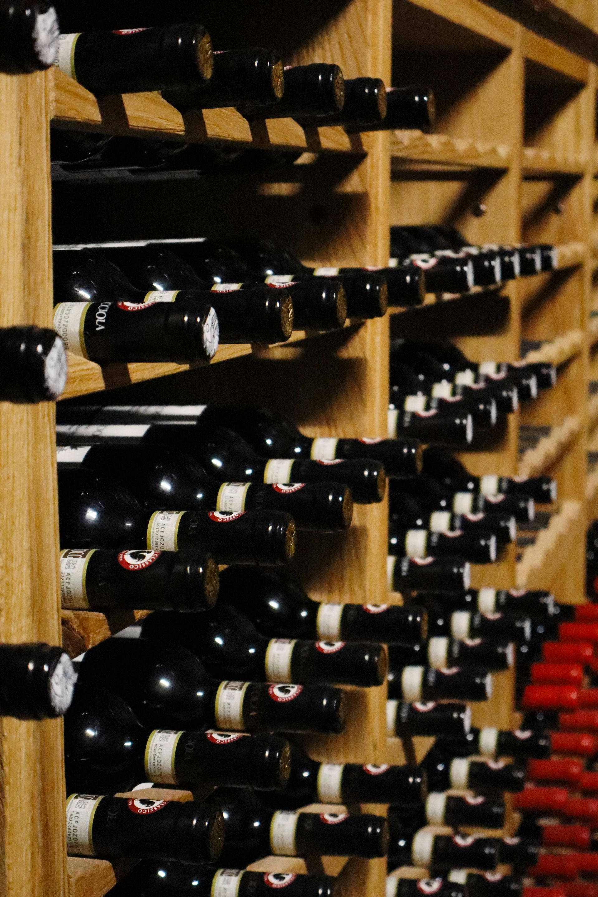 Wine bottles with dark labels neatly arranged on wooden racks in a storage cellar.