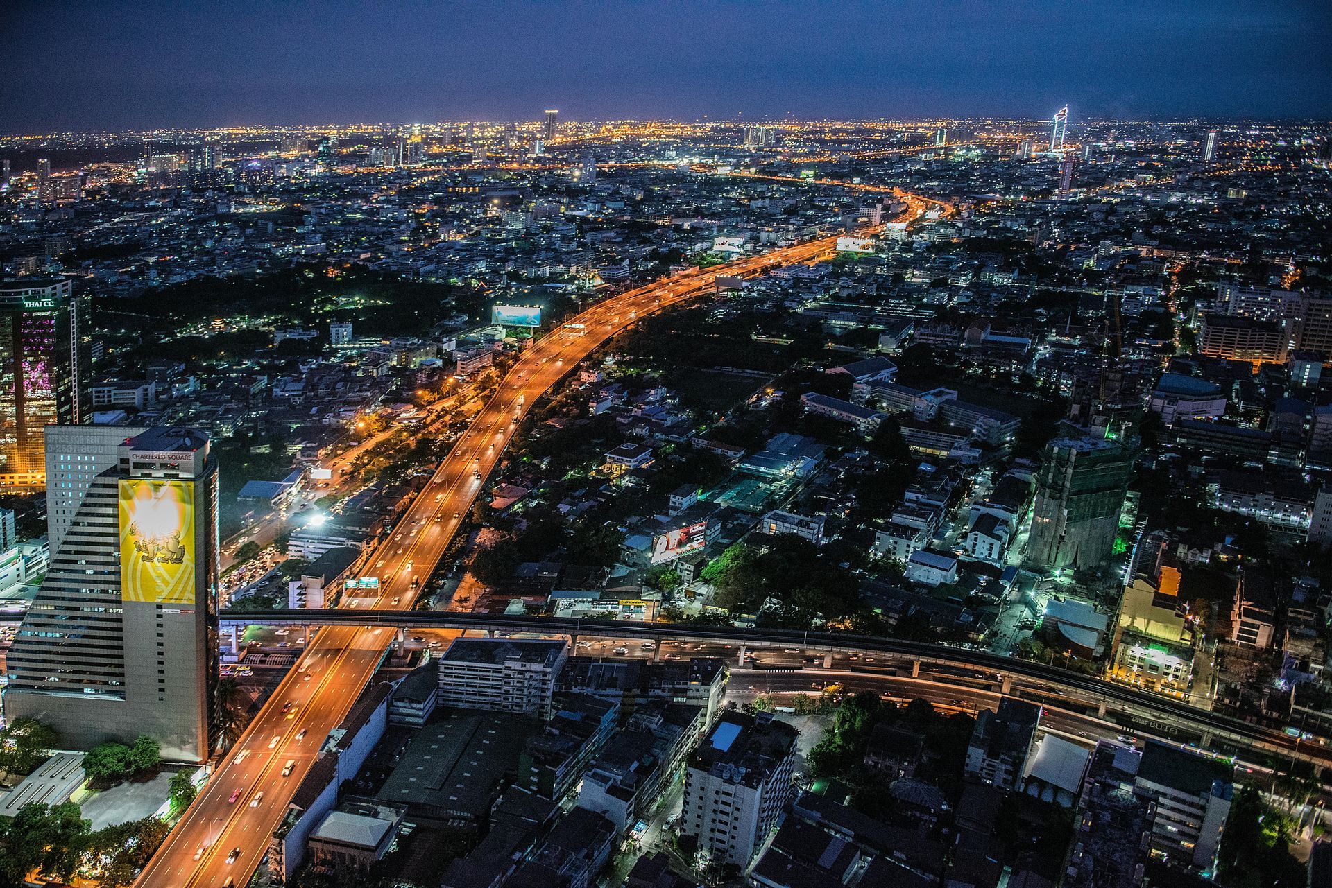 City skyline at night with bright lights along a highway, buildings, and dark sky.