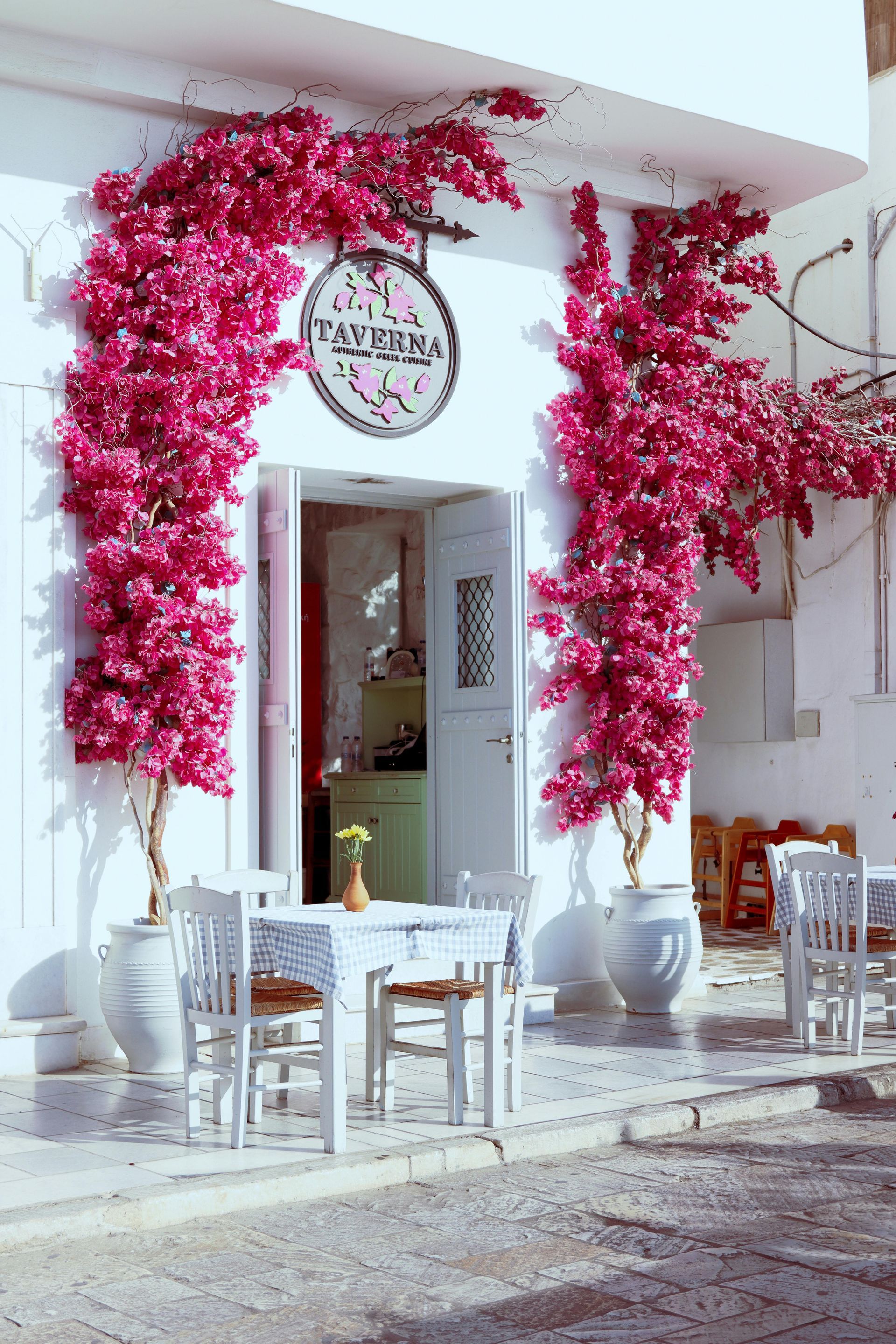 Pink floral arch framing a white café entrance with outdoor tables and chairs Naxos