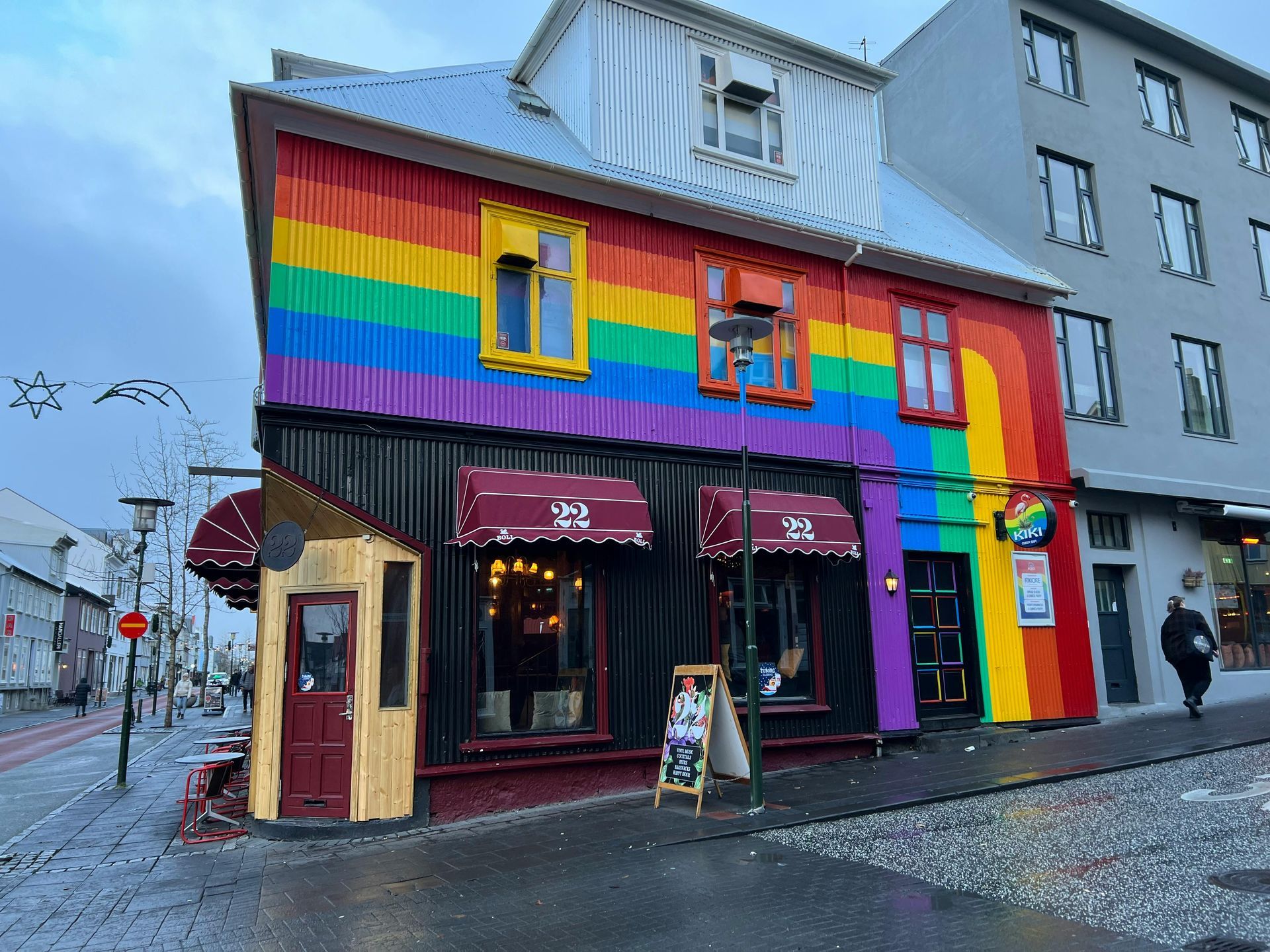 Rainbow-colored building in a city street with a restaurant; a person walks on the sidewalk. Reykjavik Pride: A Nordic Gem