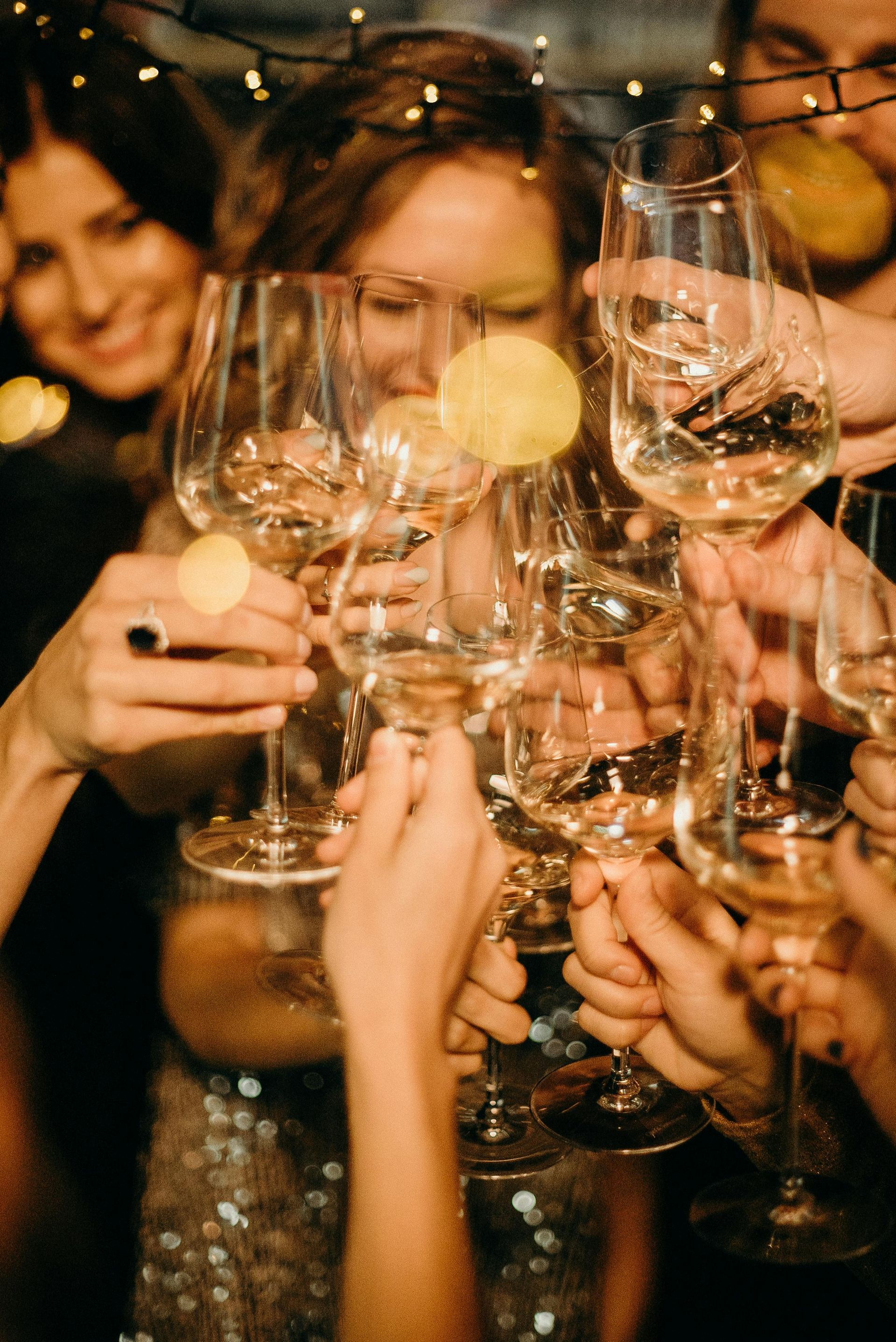 People toasting with champagne glasses at a party, illuminated by string lights.