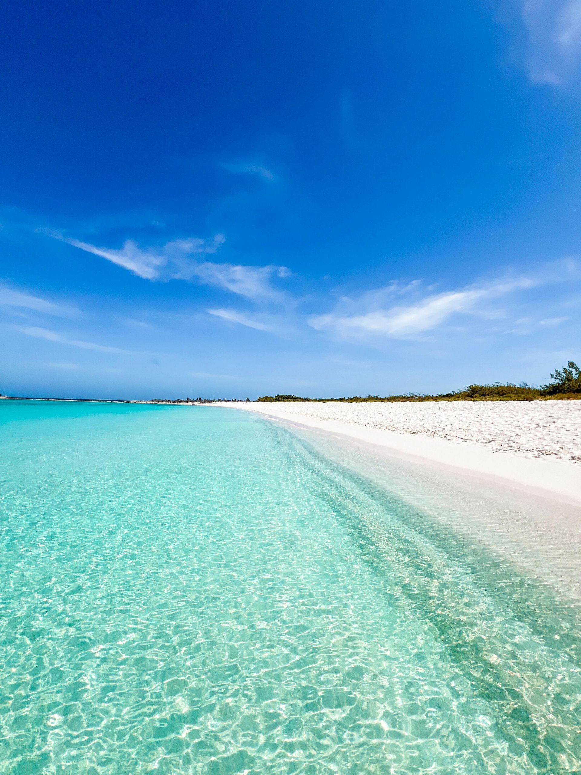 Turquoise water washes onto a white sand beach under a bright blue sky.