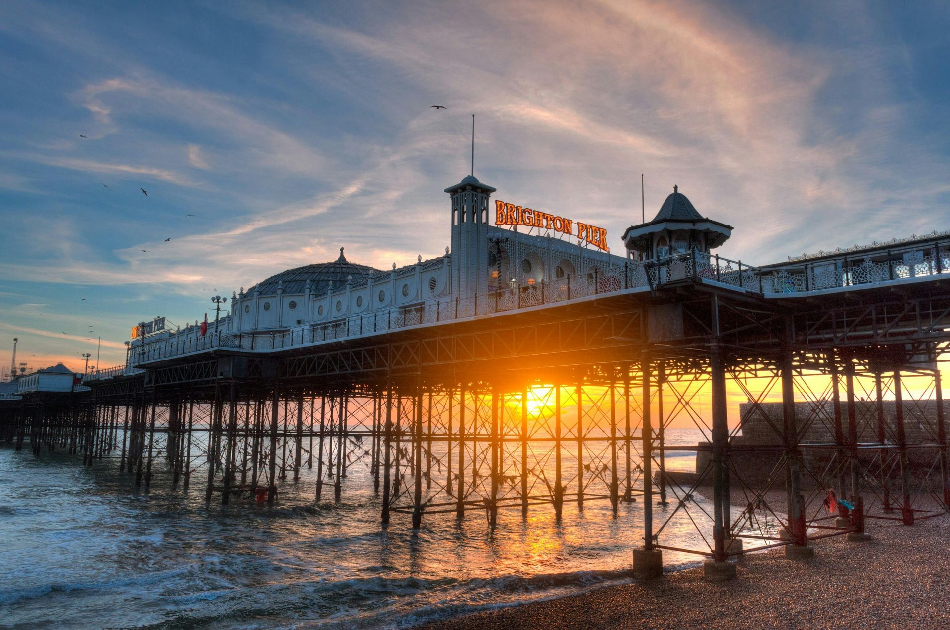 Brighton Palace Pier at sunset, silhouetted against a colorful sky, with the sun reflecting on the water.