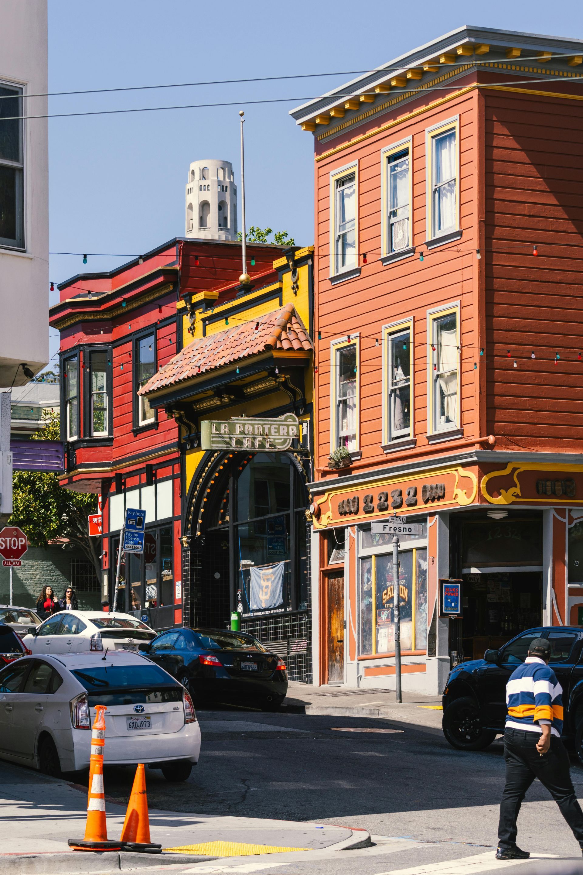 Colorful historic buildings line a steep city street with parked cars and traffic cones.