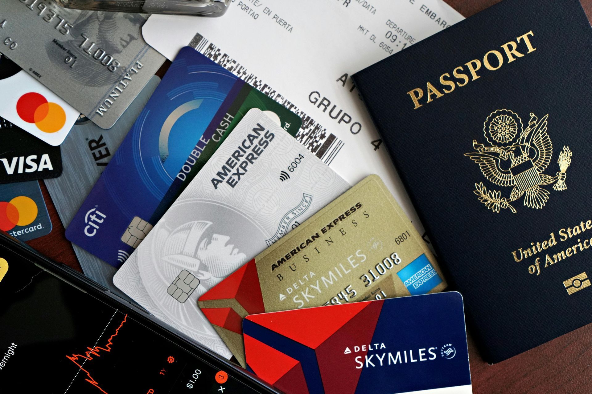 Pile of credit cards, passport, and receipts. Includes a Delta SkyMiles card, American Express cards, and a smartphone.