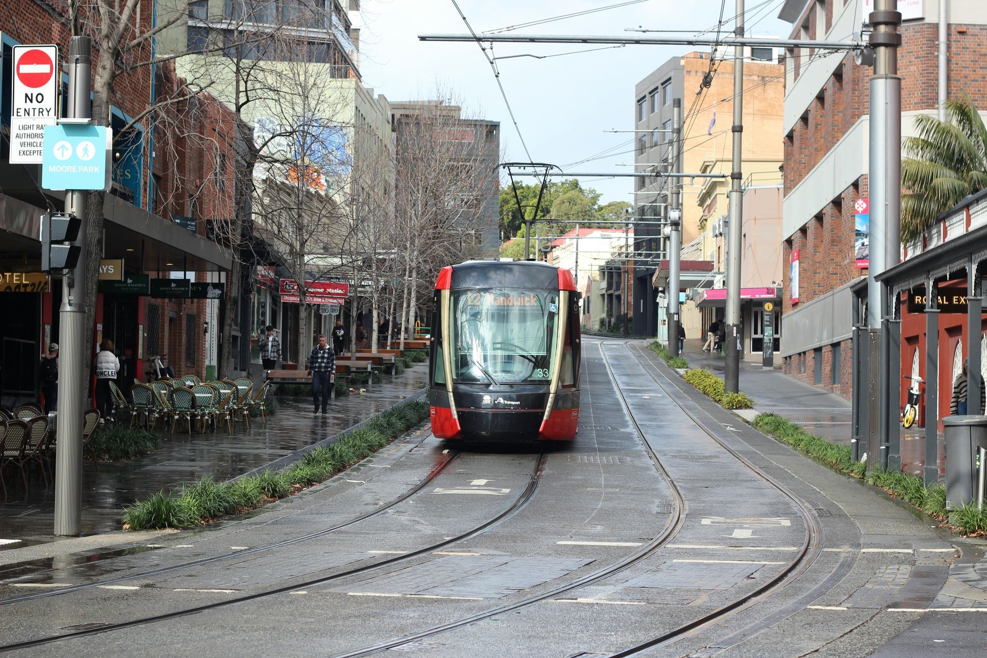Tram traveling down a wet street in a city with shops on either side. Darlinghurst Syndey