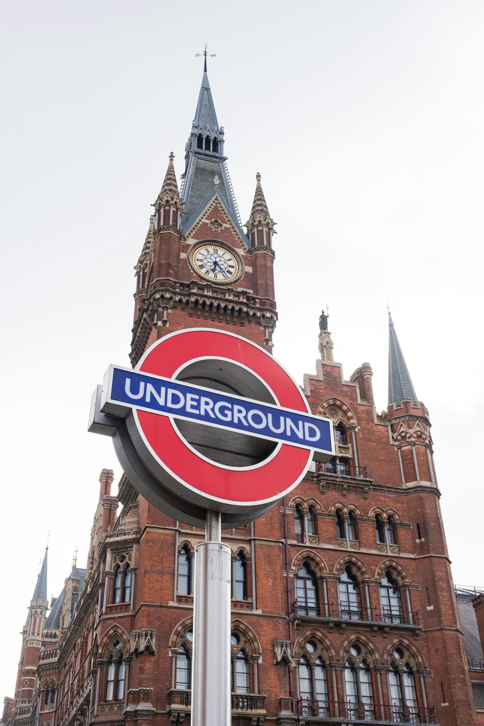 London Underground sign in front of St. Pancras station's brick facade.