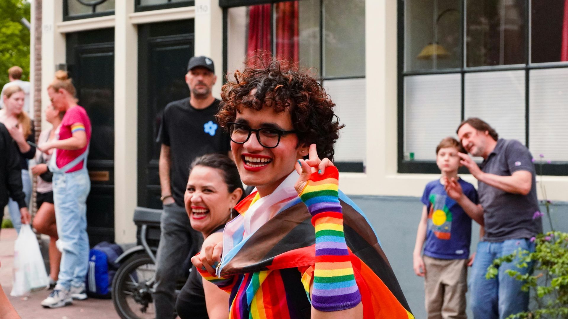 Person with rainbow flag gestures joyfully during a pride event in Amsterdam, surrounded by others. Amsterdam Pride: Pride on the Canals