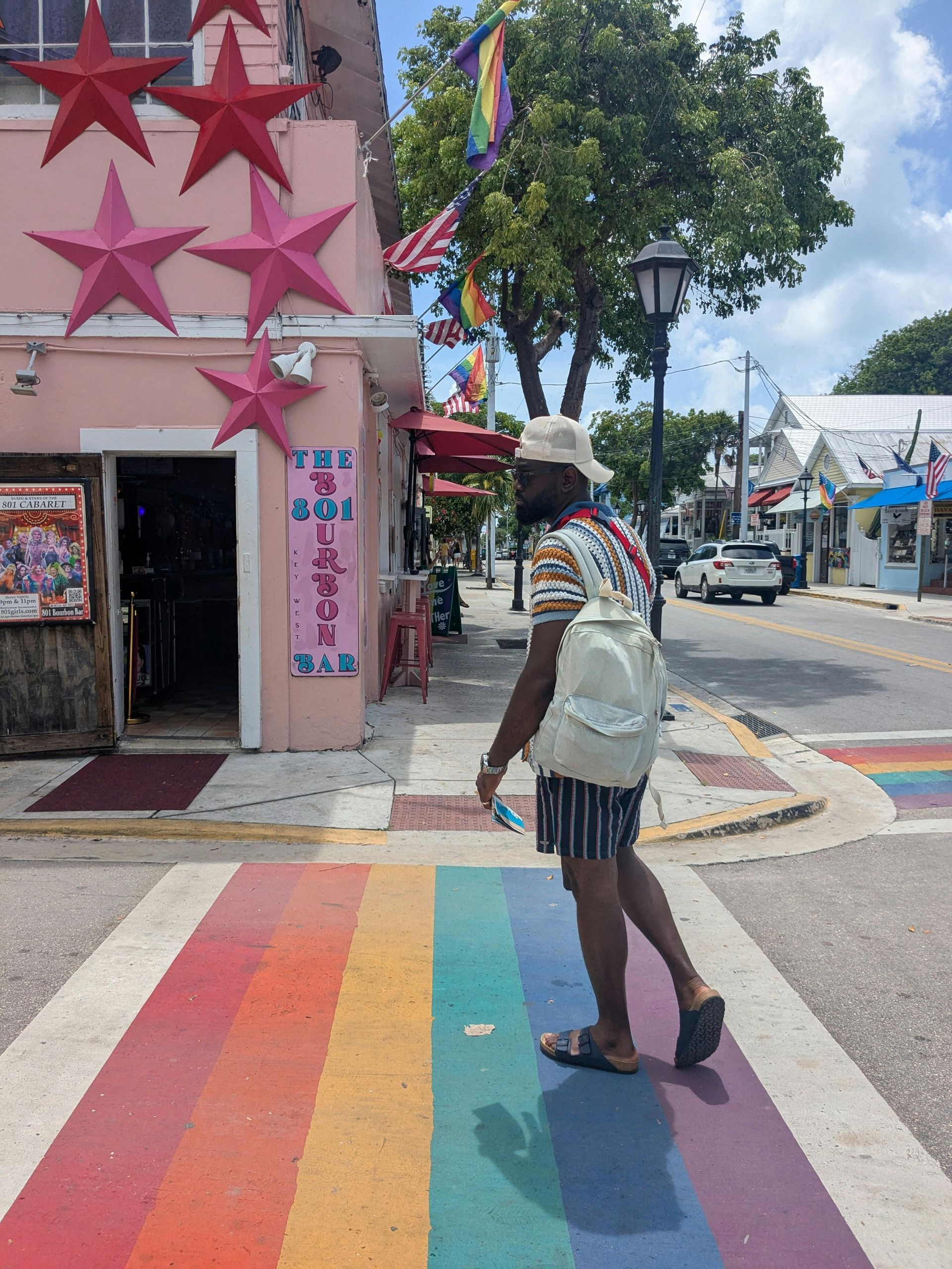 A person walking on a rainbow crosswalk in Key West. Pink building with star decor, gay pride flags.