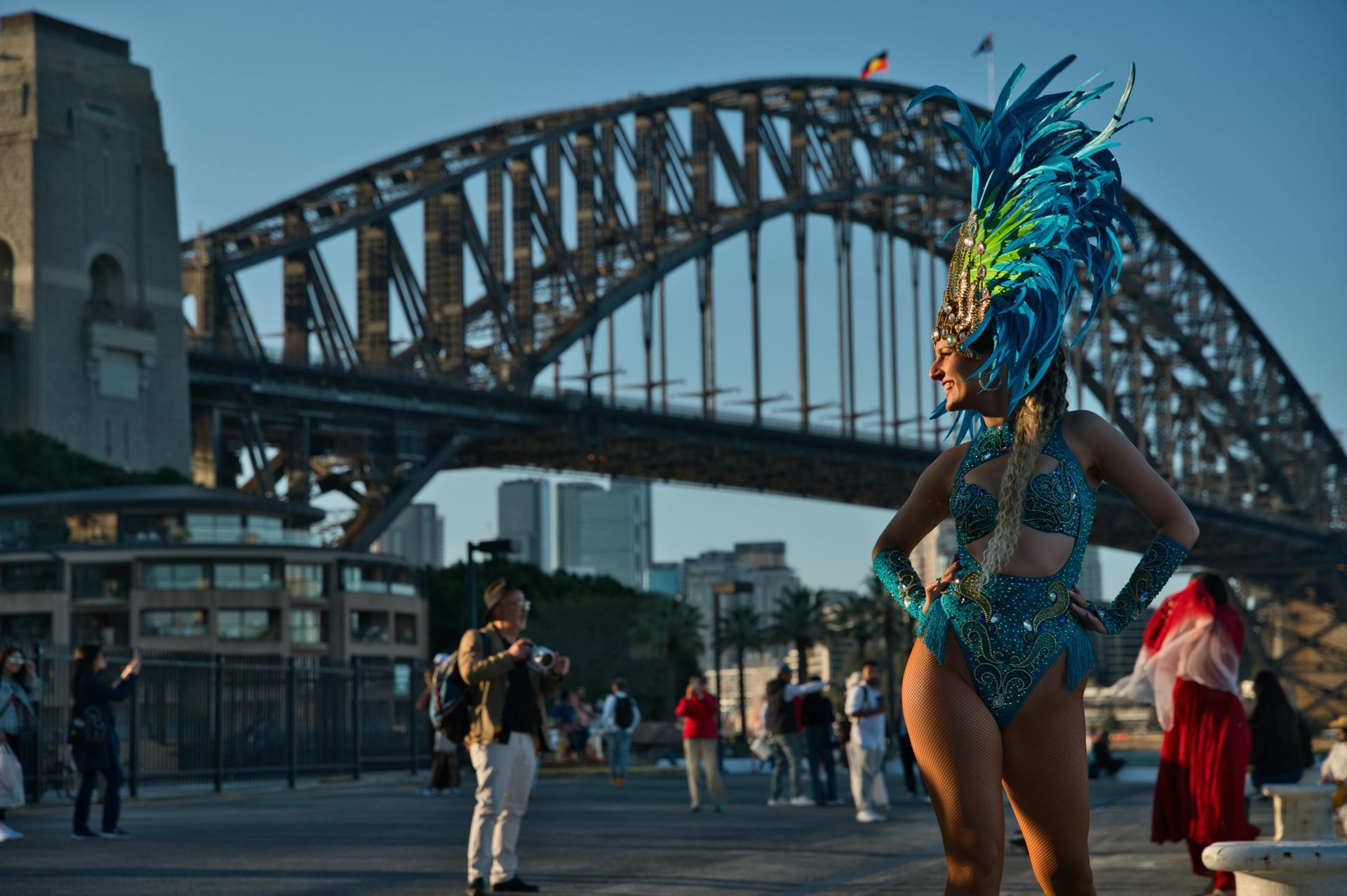 Woman in a blue and green sequined costume poses near the Sydney Harbour Bridge.