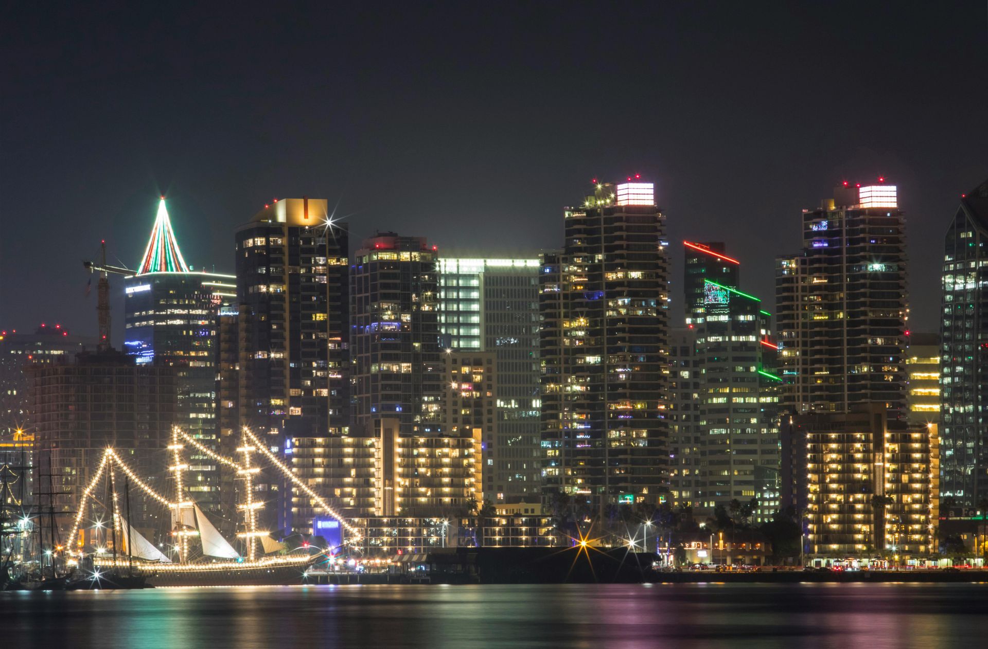 Night view of San Diego skyline, with illuminated buildings reflecting in the water, and a lit-up ship in the foreground.