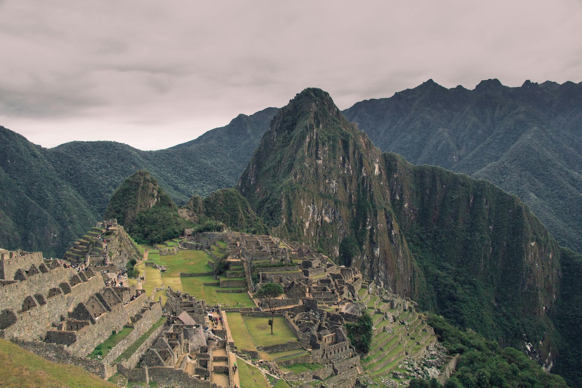 Machu Picchu ruins nestled in green mountains under a cloudy sky.