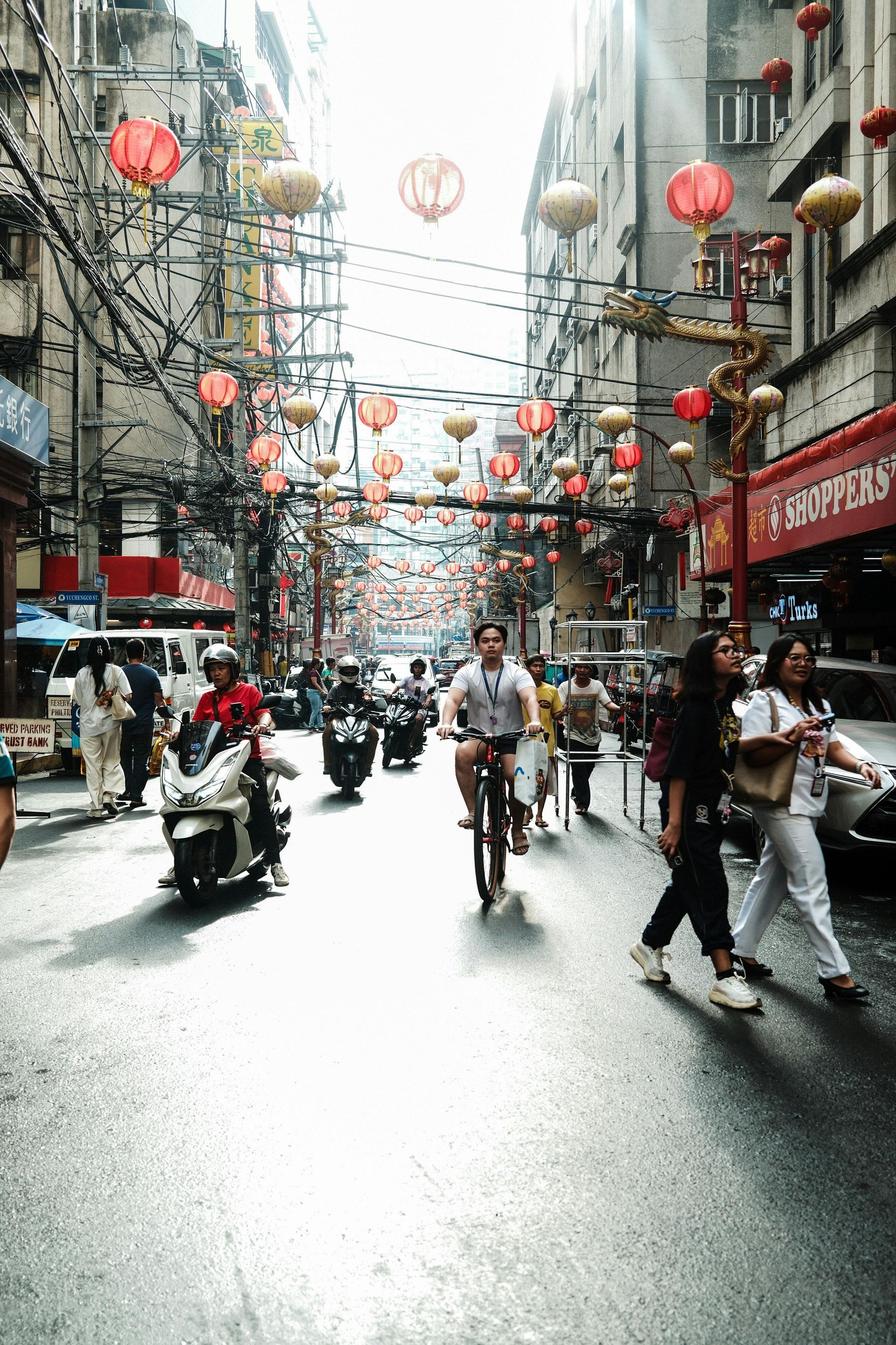A group of people sits along a stone wall at Ulun Danu Beratan Temple in Bali, with tiered pagodas and mountains behind.