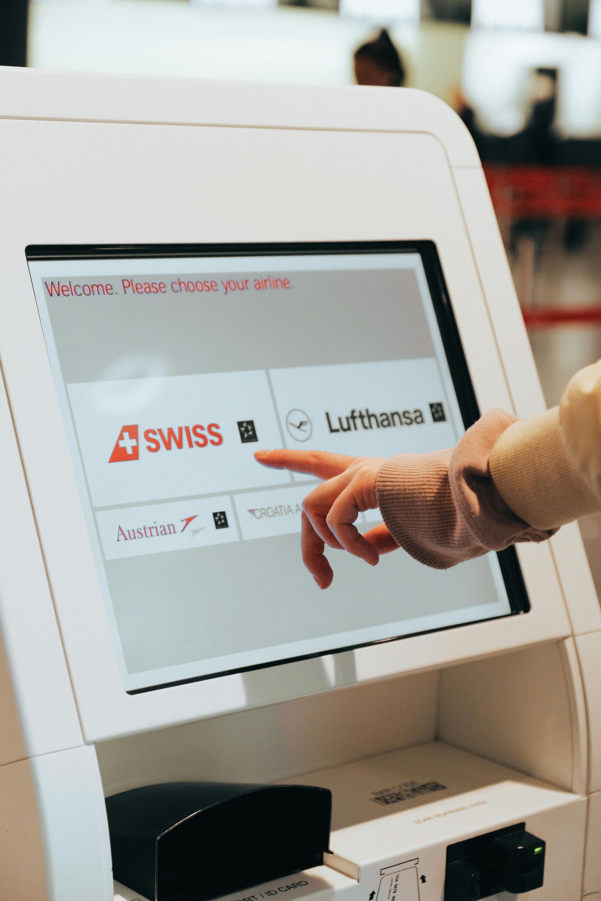 Person's hand pointing at Swiss airline logo on a self-service kiosk screen at an airport.