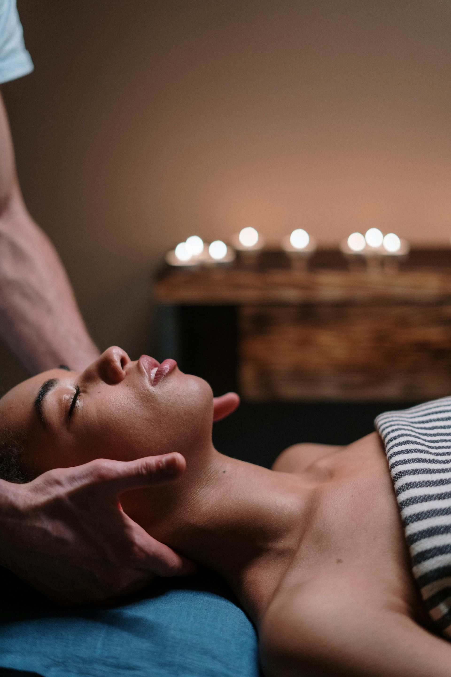 Woman receiving neck massage, eyes closed, candles in background.