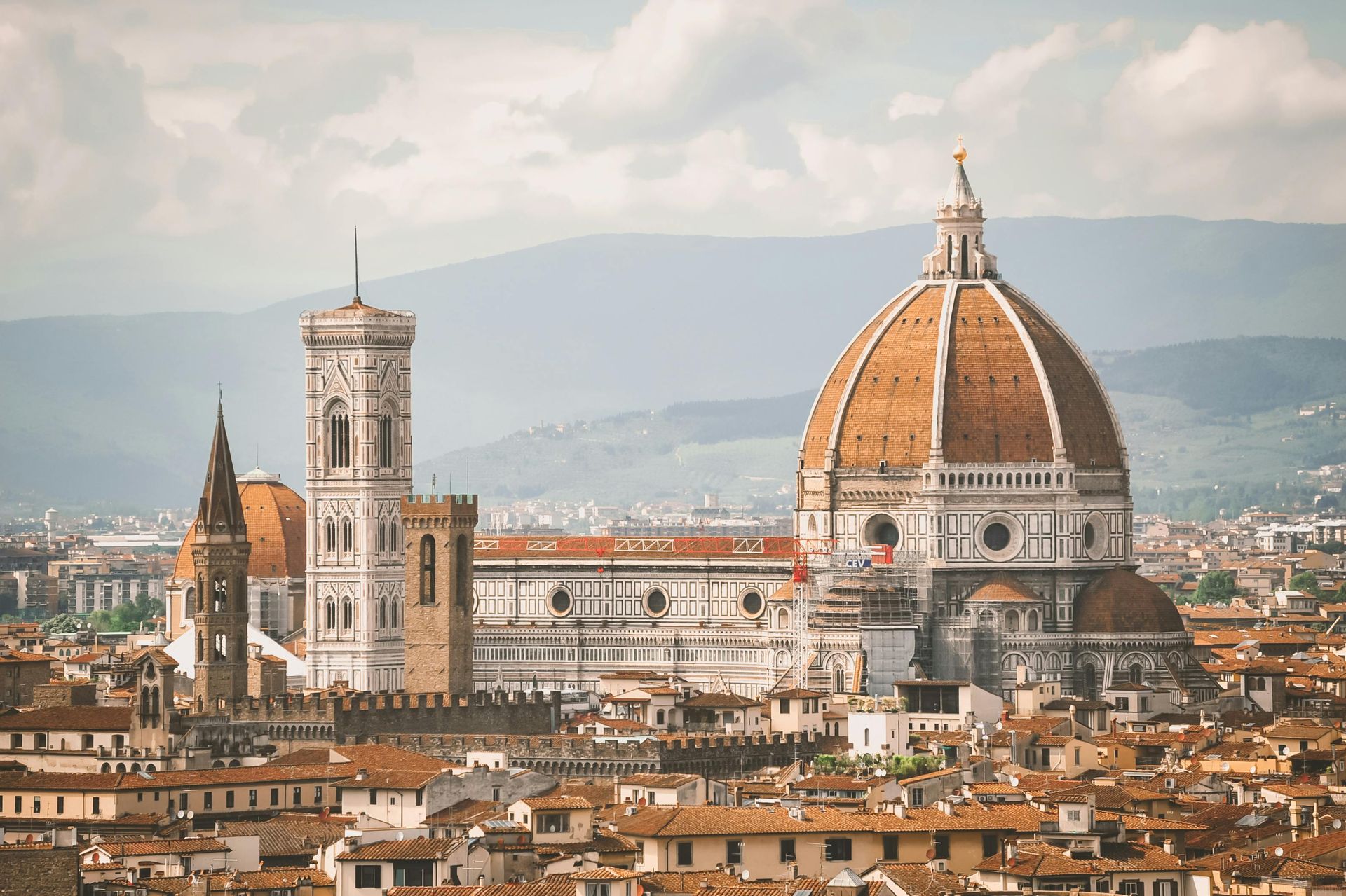Florence Cathedral and surrounding buildings with a reddish-brown dome under a cloudy sky.