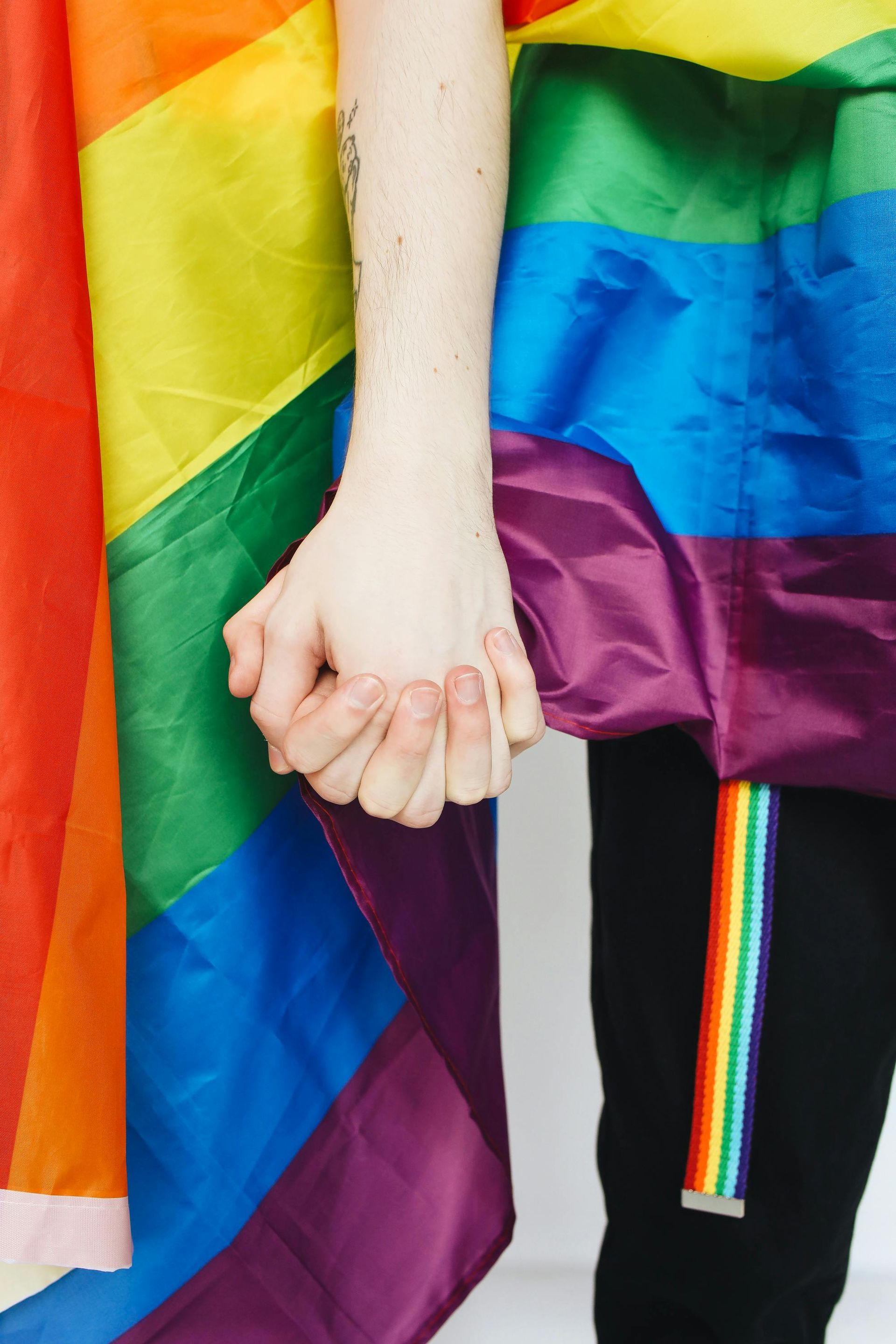 People holding hands, draped in a rainbow flag, with a matching rainbow belt.