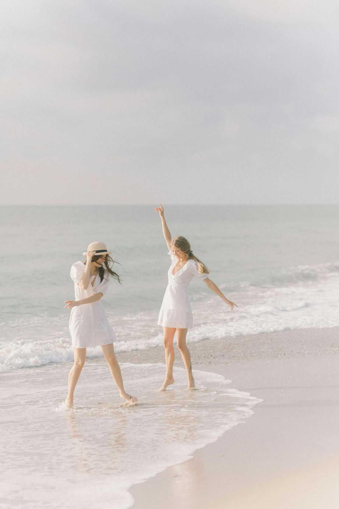 Two women in white dresses are standing on a beach.