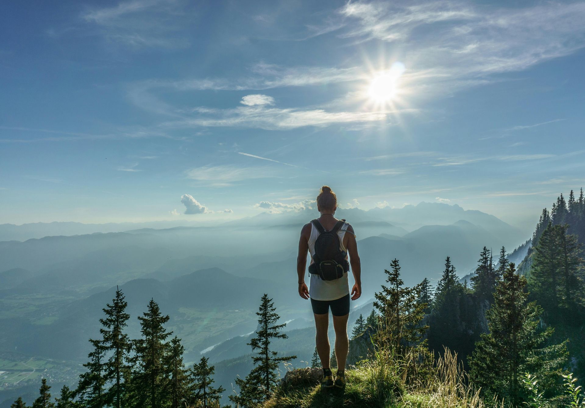 Hiker standing on a mountain overlook at sunrise with hazy blue peaks and pine trees below