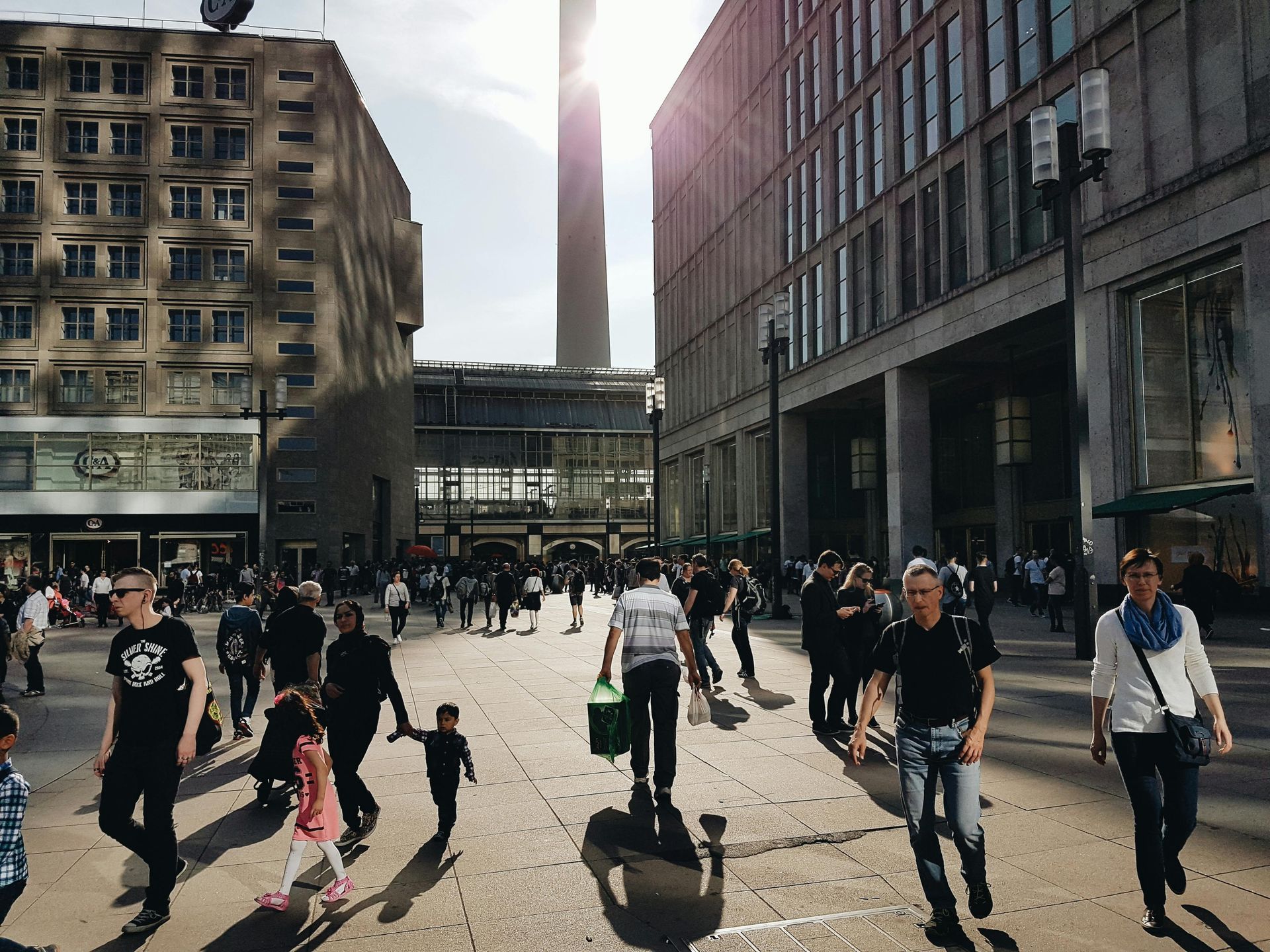 People walking in a city square with tall buildings and a distant tower. Sunny day.Schöneberg – Berlin