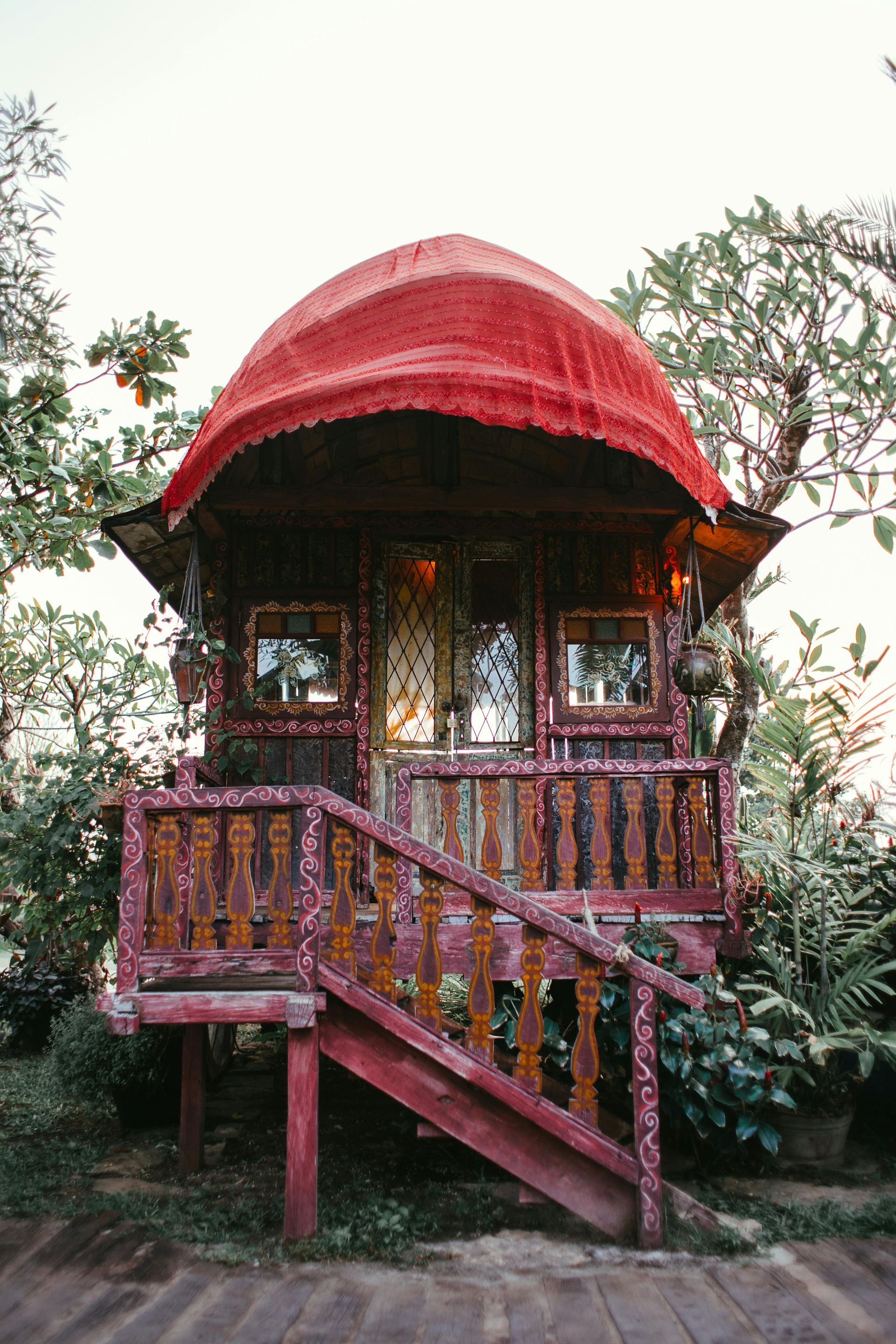 Red-painted wooden cabin with an arched roof and porch, surrounded by greenery.