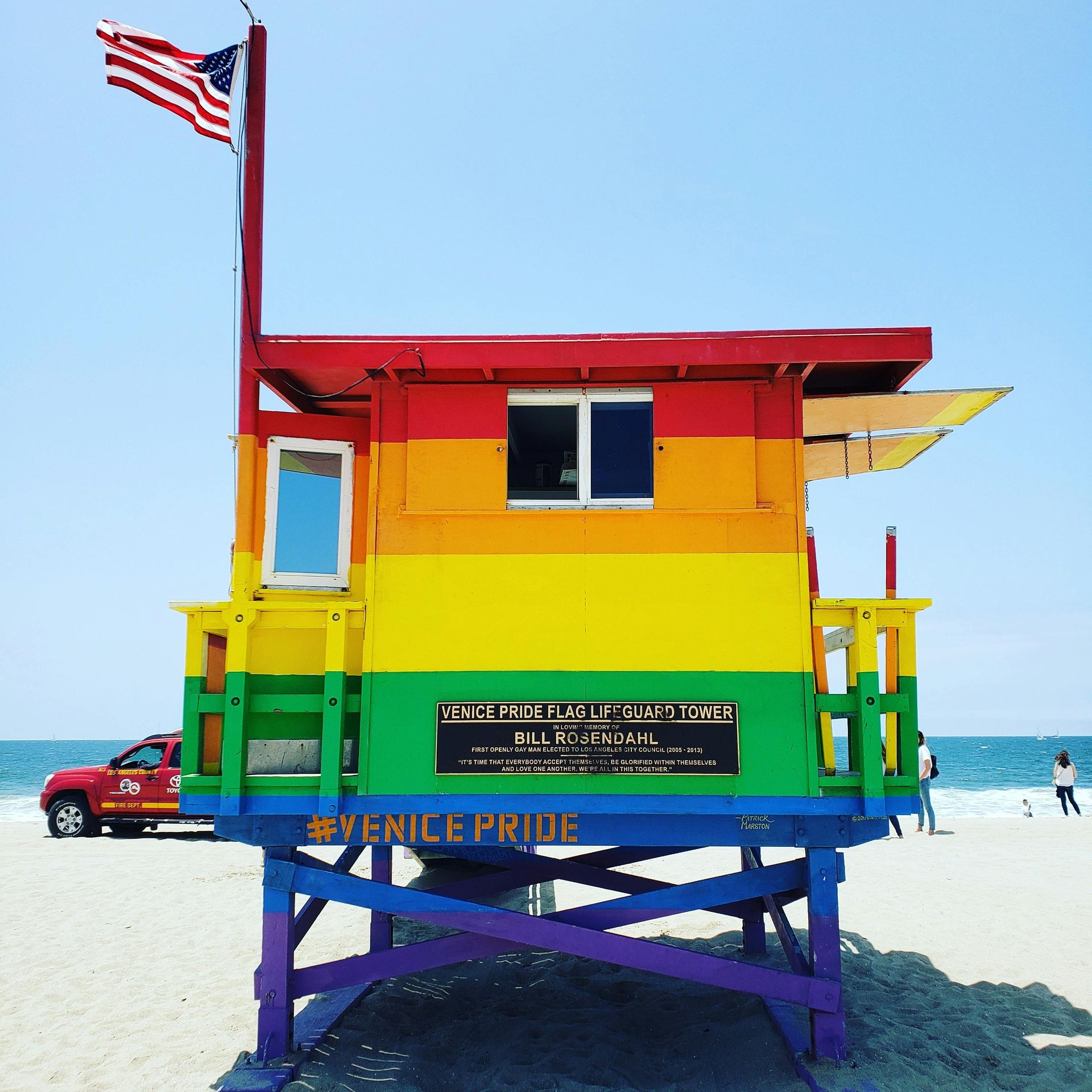 Rainbow-colored lifeguard stand on a beach with an American flag.