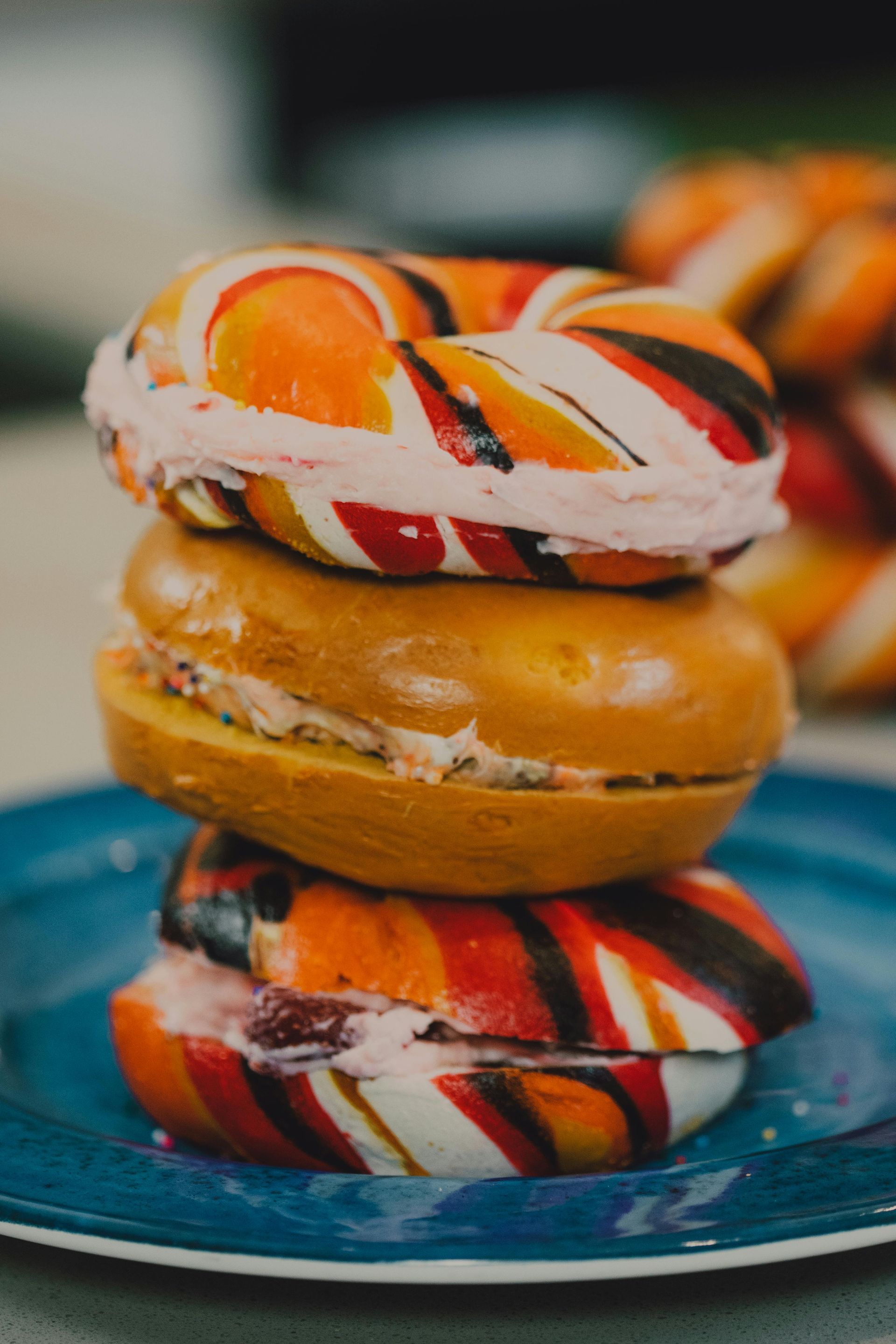A stack of three bagels with pink cream cheese filling on a blue plate; two bagels have a swirled orange, red, and black.