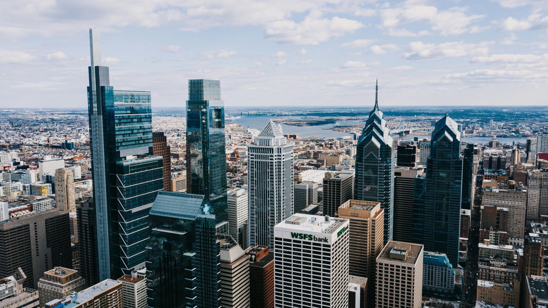 Aerial view of Philadelphia skyline with tall glass skyscrapers and a blue sky.