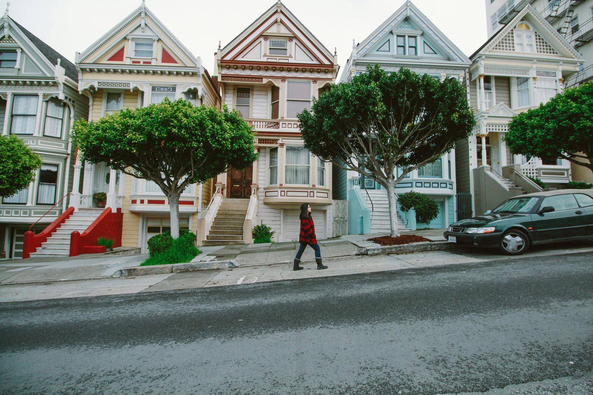 Row of colorful Victorian houses in San Francisco with a person walking on the sidewalk in front. San Francisco