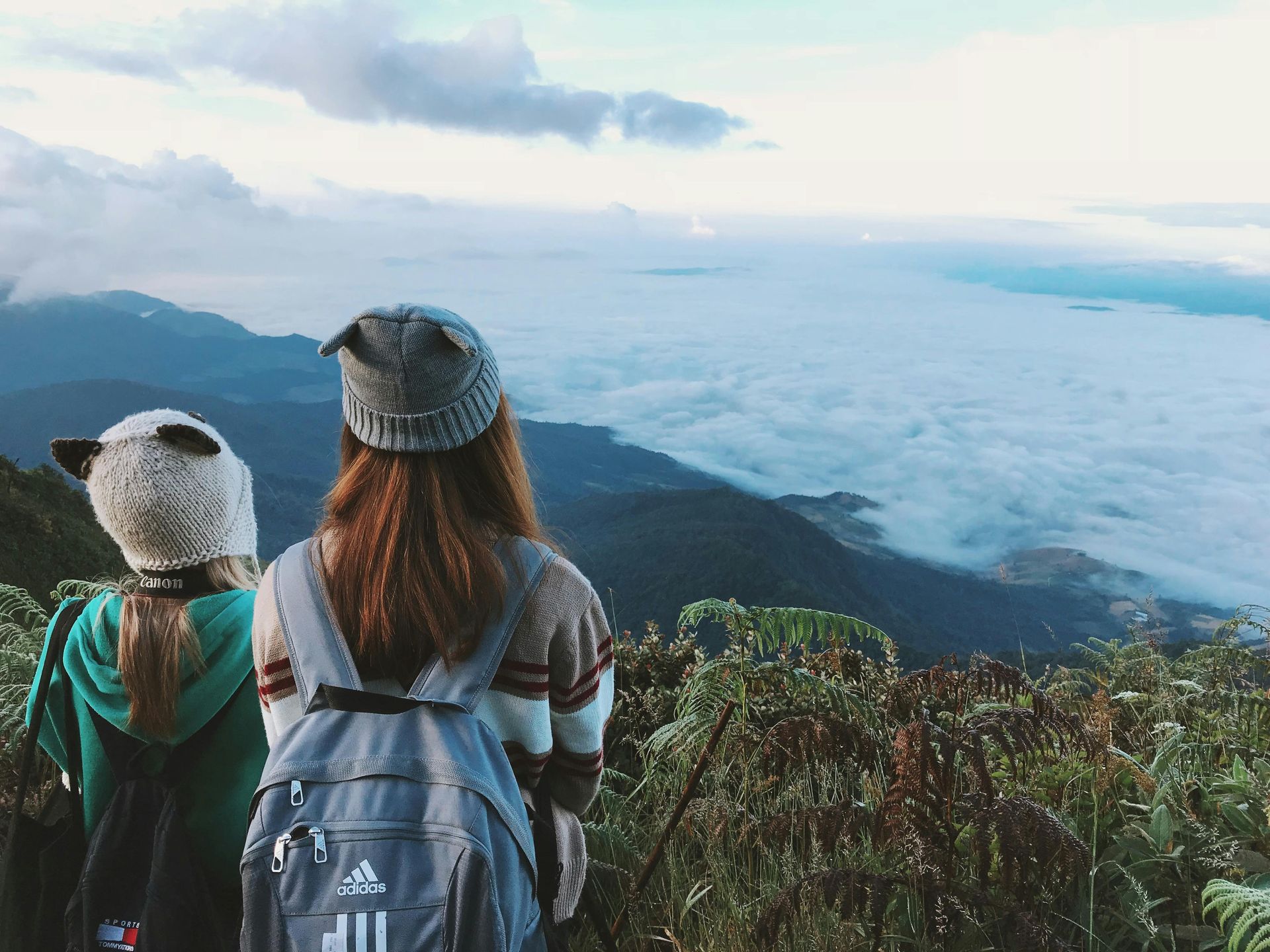 Two people with backpacks on mountain, looking at fog-filled valley. Chiang Mai,