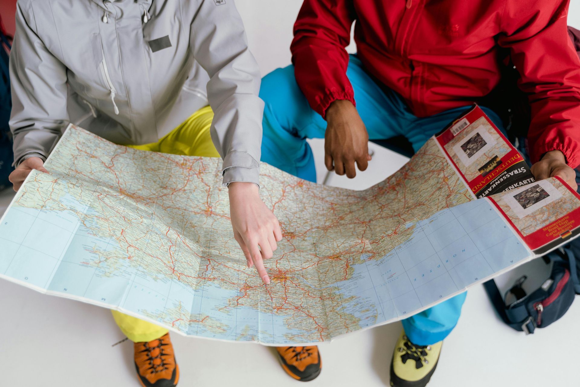 Two people pointing at a map; one in gray jacket, one in red, seated.