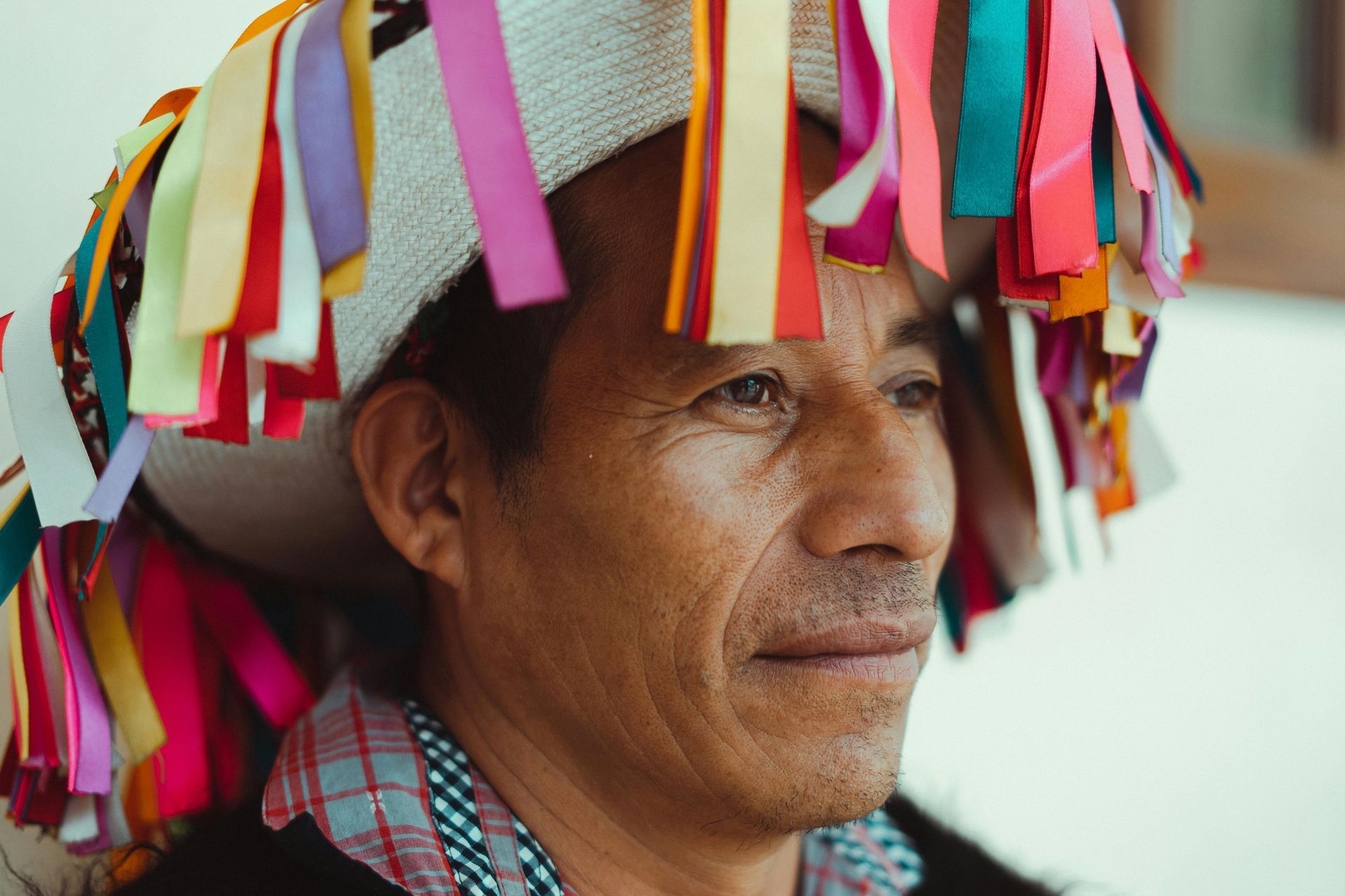Man wearing a hat adorned with colorful ribbons, looking to the side.