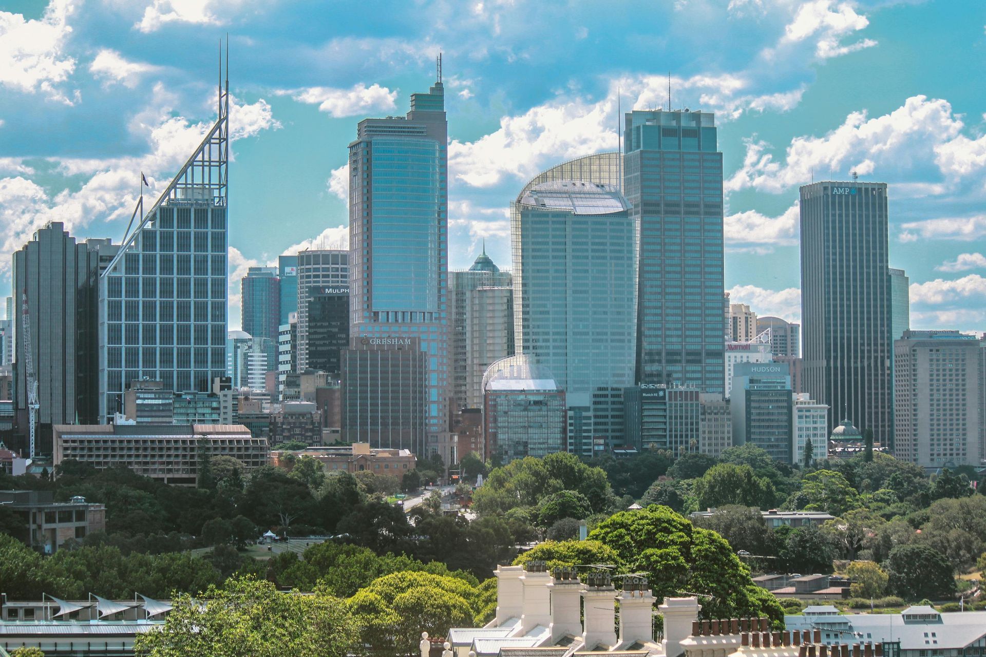City skyline with skyscrapers against a blue sky, trees in foreground.