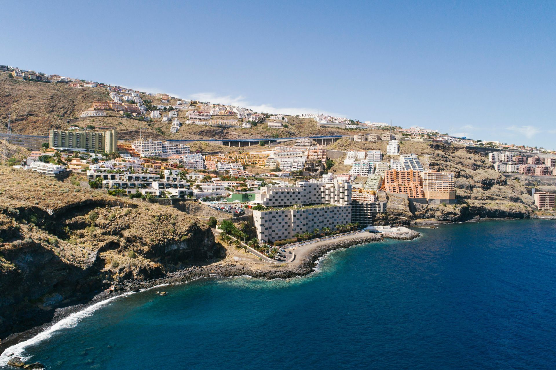 Coastal town on a sunny day, with buildings on the hillside and deep blue sea.