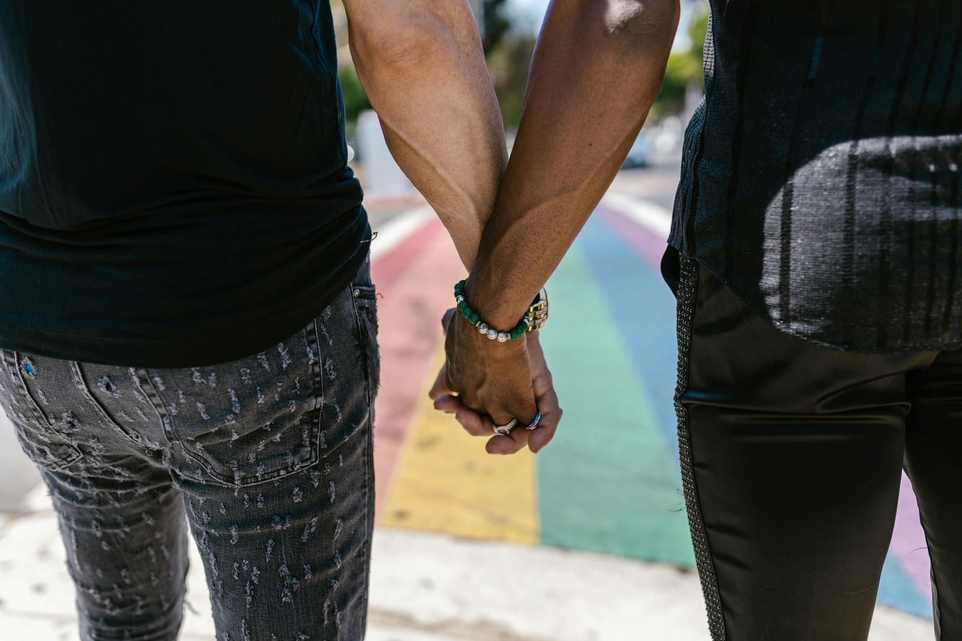 Two people holding hands while standing on a rainbow-painted crosswalk.
