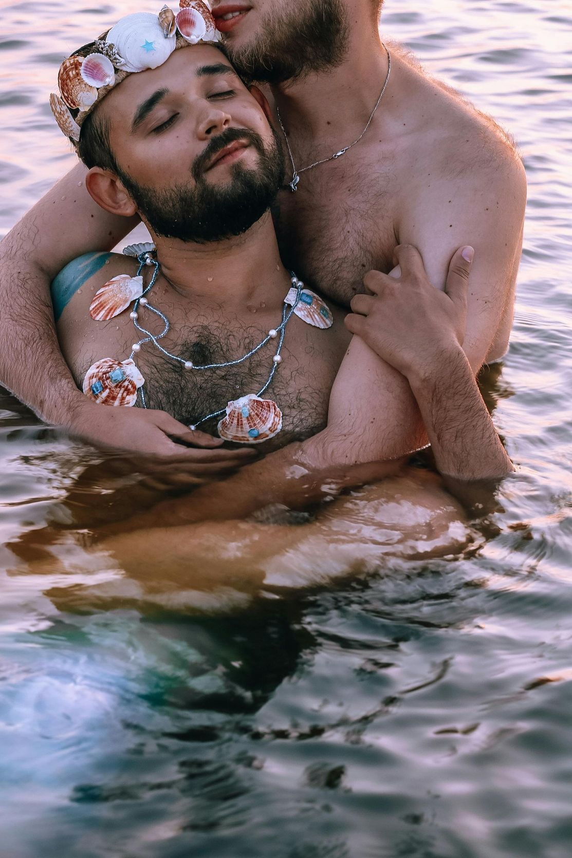 Two men are hugging each other in the water . one of the men is wearing a crown.