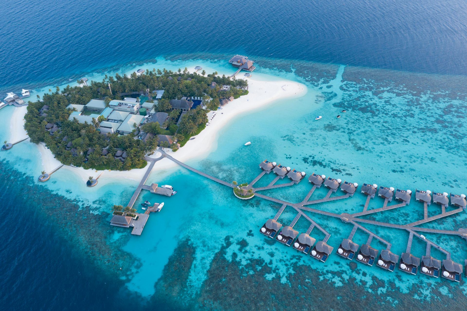 Aerial view of a tropical island resort. Turquoise water surrounds the island with overwater bungalows and lush vegetation. maldives