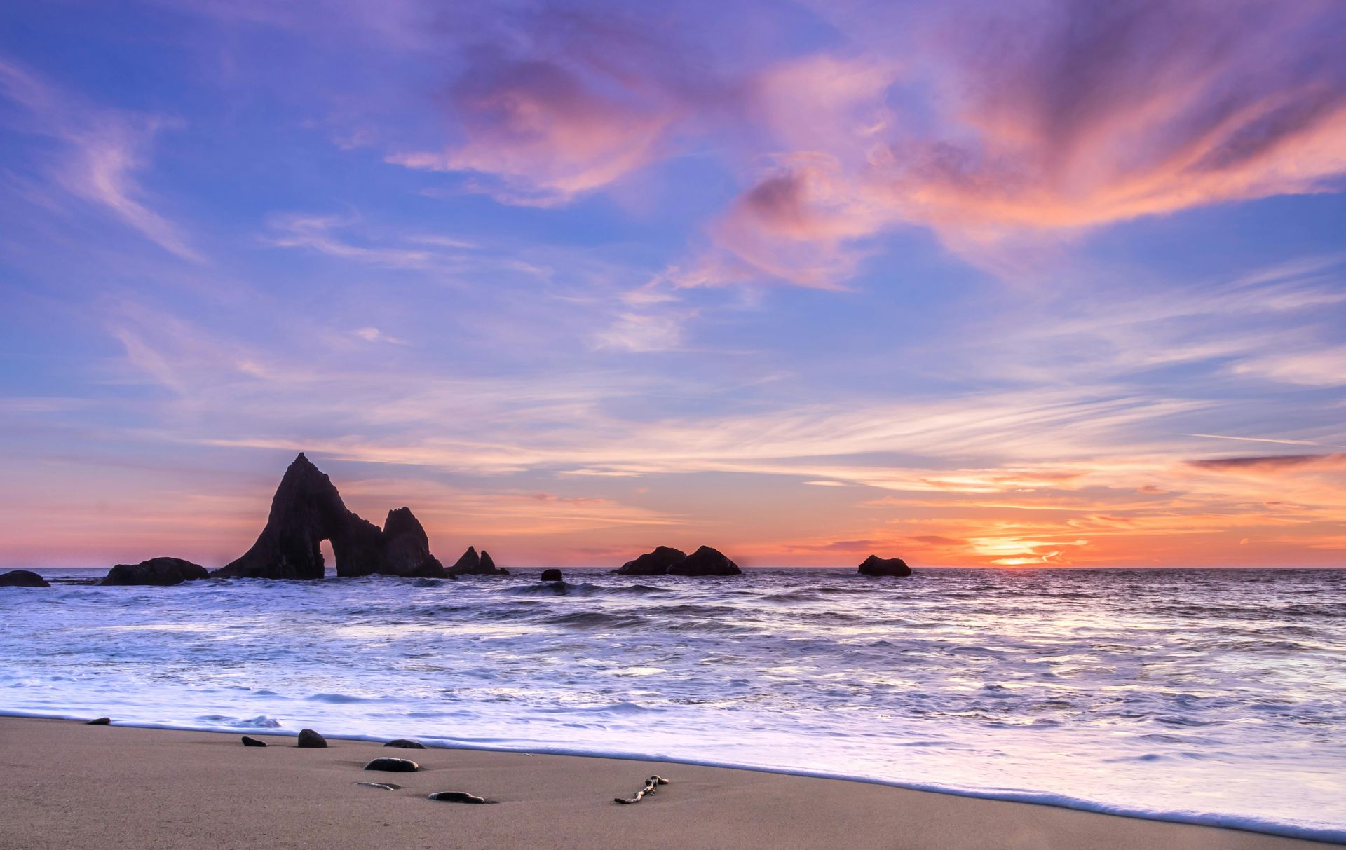 Sunset over ocean with rocky islands; pink and purple sky reflecting in the water.California