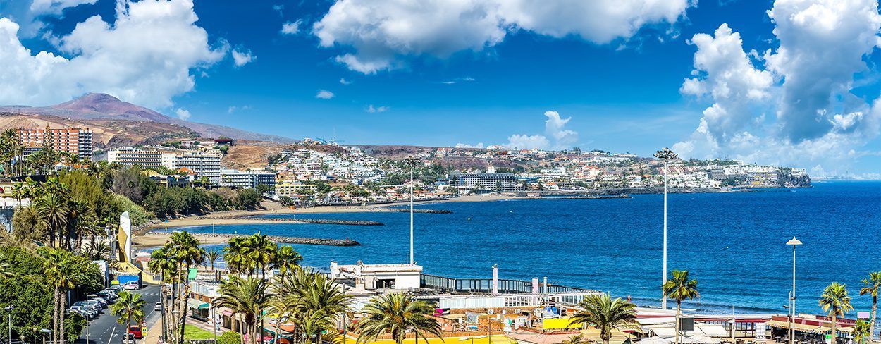 Coastal town with blue water under a clear sky with fluffy white clouds. Playa del Inglés
