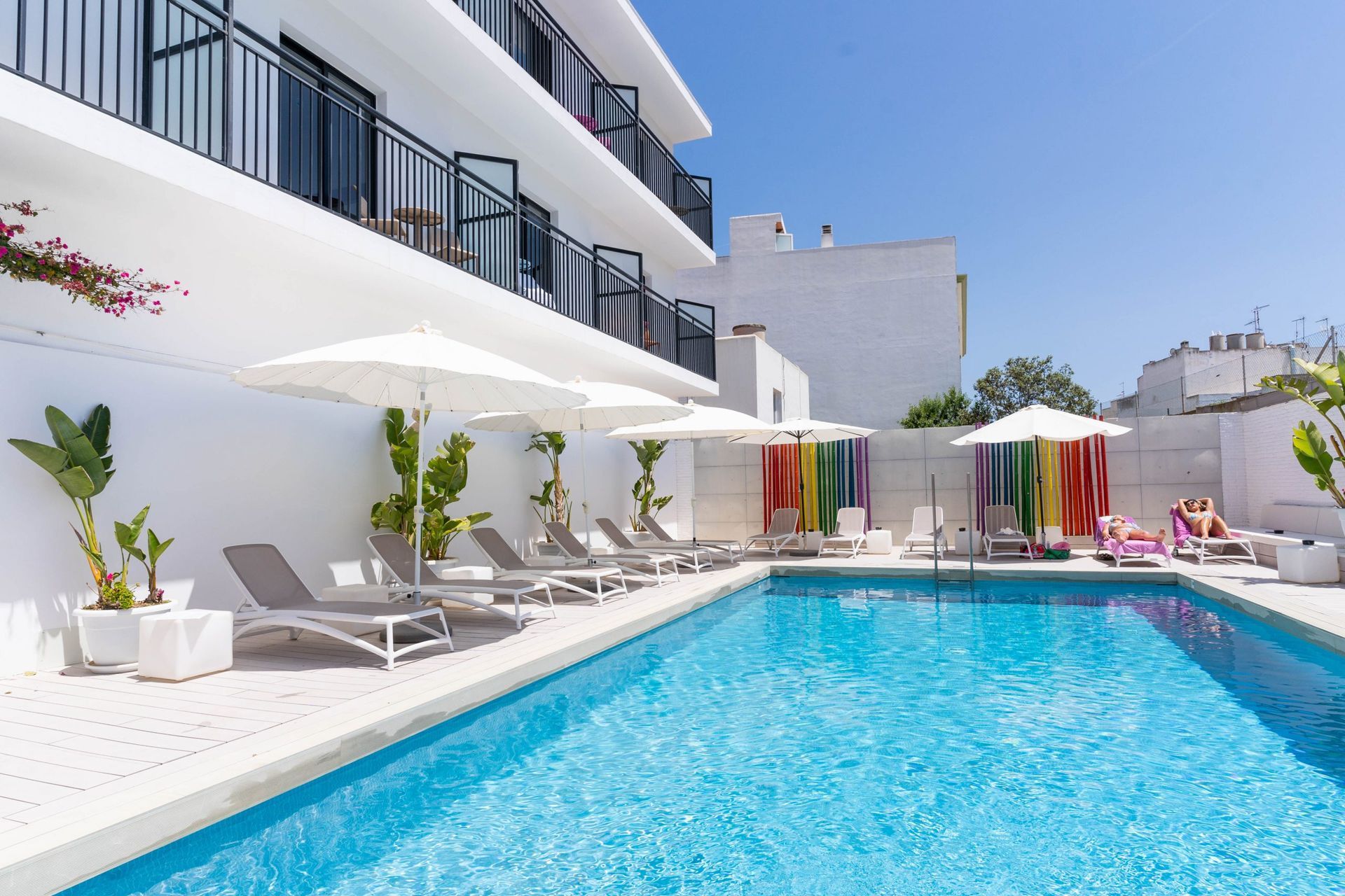 A large swimming pool surrounded by chairs and umbrellas in front of a hotel.