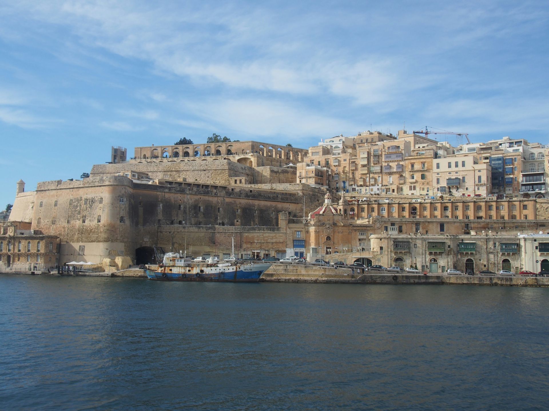 Coastal cityscape with stone buildings and fortifications under a blue sky.