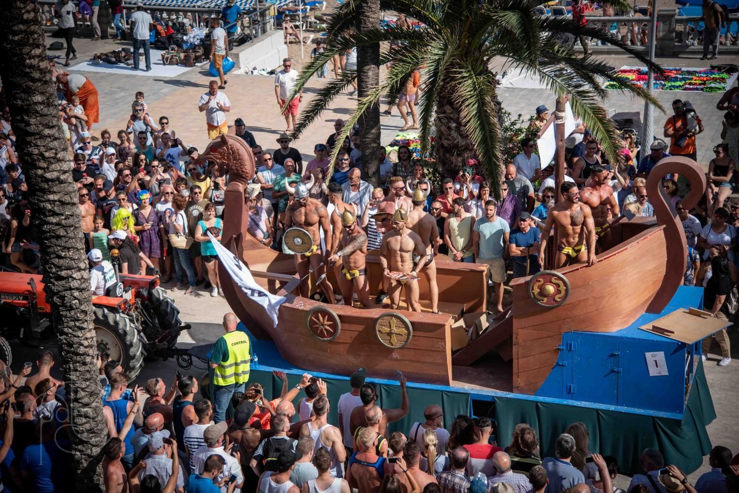 Festival parade with people in a Viking boat float; sunny outdoor setting, many onlookers. Barcelona sitges pride
