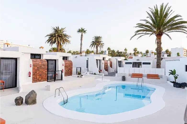 A large swimming pool surrounded by palm trees in front of a white building.