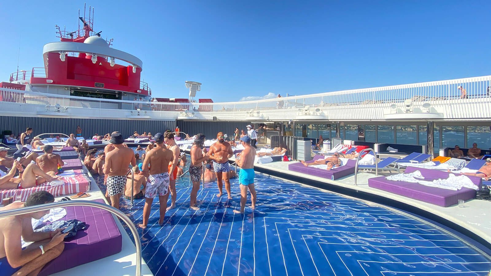 People relax and socialize in and around a blue tiled swimming pool on the sun-drenched deck of a cruise ship. Atlantis Brilliant Lady LA
