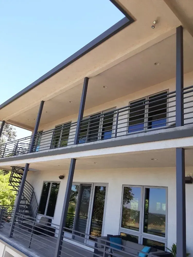 Modern two-story building with balconies, gray columns, and tinted windows under a clear sky.
