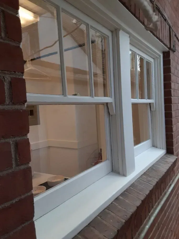 White-framed windows with panes in a brick building. Window sill visible. Interior is bright.